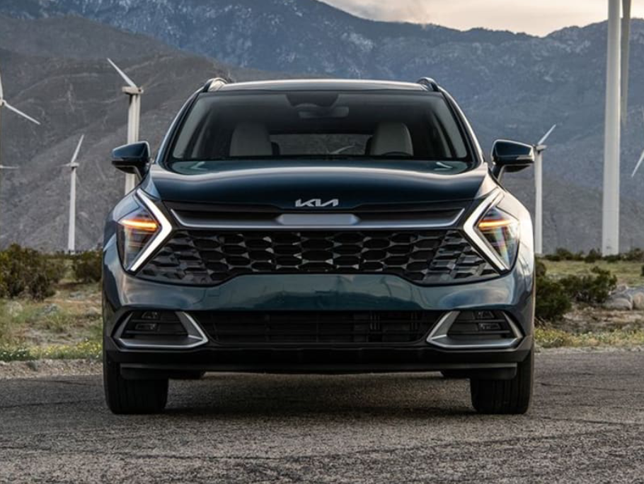 A dark Kia SUV parked in front of wind turbines
